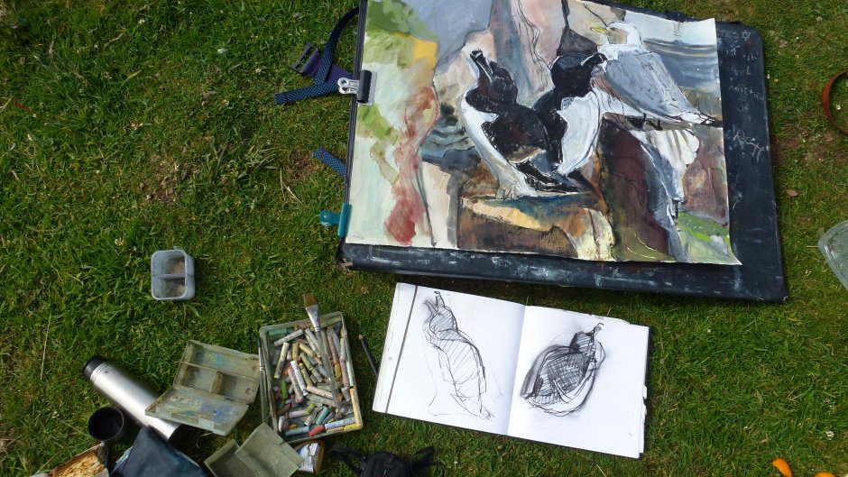 Artist set up working outdoors, drawing, sketches and materials laid on grass